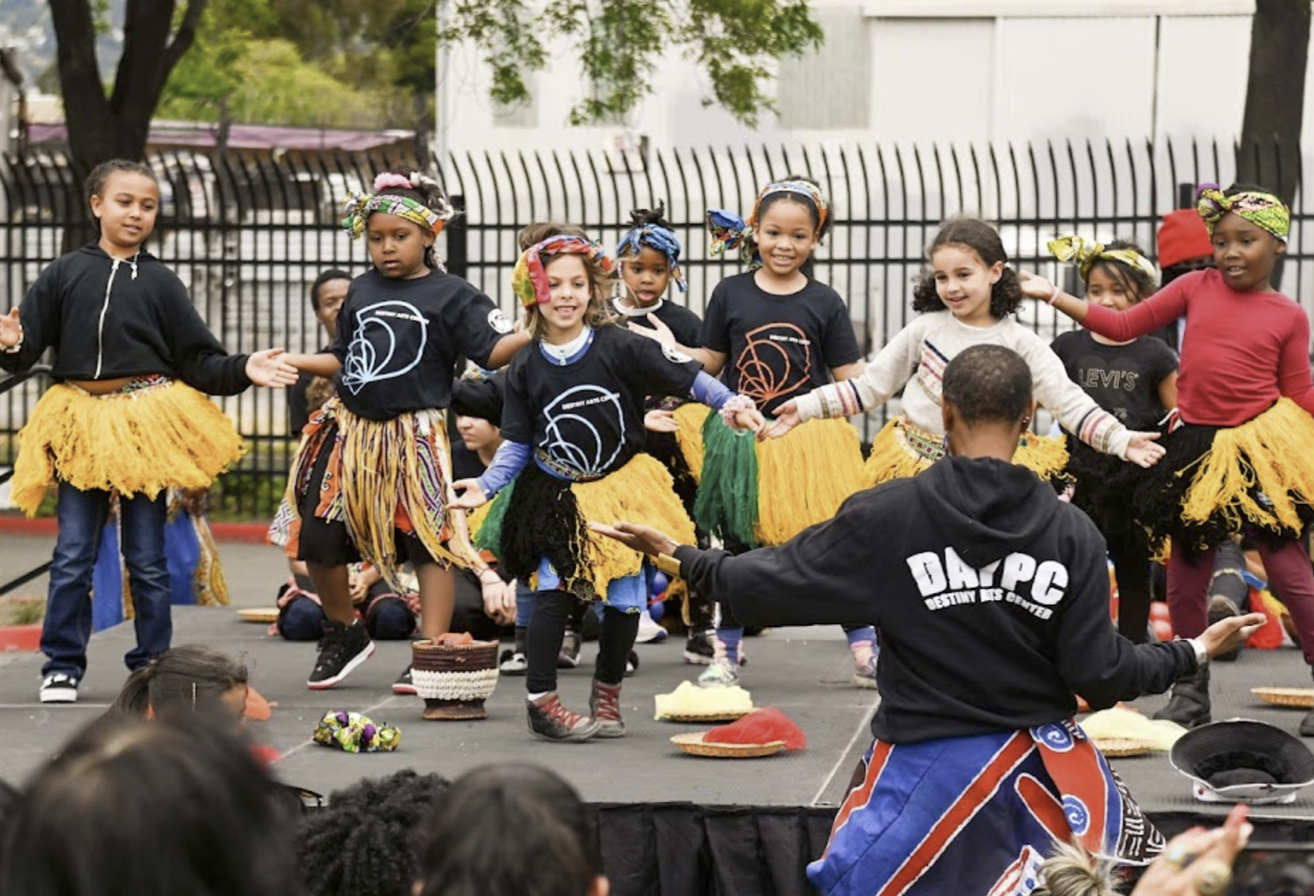 Youth on stage performing African dance with an instructor wearing DAYPC sweatshirt facing the youth.